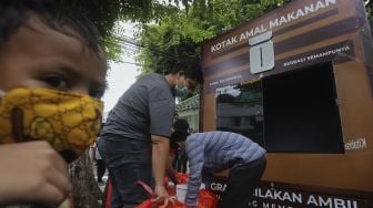 Seorang anak mengantre untuk mengambil makanan gratis di Kotak Amal Makanan Gratis di pelataran Masjid Cut Meutia, Jakarta, Jumat (11//12/2020). [Suara.com/Angga Budhiyanto]