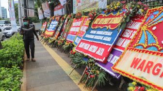 Warga melintas didepan Karangan bunga yang membanjiri halaman depan Polda Metro Jaya, Jakarta Selatan, (12/12). [Suara.com/Alfian Winanto]