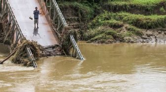 Seorang warga berkomunikasi jarak jauh dari jembatan penghubung yang putus pasca diterjang banjir susulan di Desa Darussalam, Kecamatan Geureudong Pase, Aceh Utara, Aceh, Minggu (13/12/2020).  [ANTARA FOTO/Rahmad]