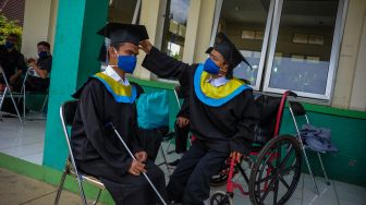 Seorang siswa disabilitas membetulkan posisi topi toga rekannya saat mengikuti wisuda di Panti Sosial Rehabilitasi Penyandang Disabilitas Dinas Sosial Provinsi Jawa Barat, Cimahi, Jawa Barat, Selasa (15/12/2020). [ANTARA FOTO/Raisan Al Farisi]