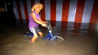 Sejumlah warga melintasi genangan banjir di Desa Tembok Lor, Kabupaten Tegal, Jawa Tengah, Jumat (1/1/2021) malam.  ANTARA FOTO/Oky Lukmansyah