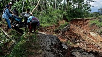 Warga mengangkat kendaraan roda dua saat melintasi jalan yang terdampak longsor, di Singajaya, Kabupaten Garut, Jawa Barat, Sabtu (9/1/2021). [ANTARA FOTO/Candra Yanuarsyah]