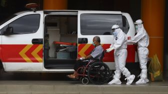 Petugas medis membantu pasien COVID-19 untuk memasuki mobil ambulans di RS Polri Kramat Jati, Jakarta, Rabu (13/1/2021). [Suara.com/Angga Budhiyanto]