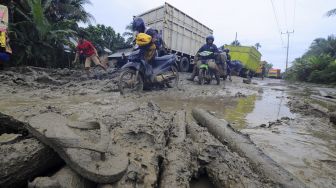 Pengendara mendorong sepeda motornya saat melintasi Jalan Lintas Jambi-Nipah Panjang yang rusak di Siau Dalam, Tanjungjabung Timur, Jambi, Rabu (14/1/2021). [ANTARA FOTO/Wahdi Septiawan]