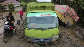 Pengendara melintas pelan di samping satu unit truk yang terperosok di Jalan Lintas Jambi-Nipah Panjang yang rusak di Siau Dalam, Tanjungjabung Timur, Jambi, Rabu (14/1/2021). [ANTARA FOTO/Wahdi Septiawan]