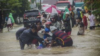 Sejumlah relawan membantu pengendara sepeda motor agar tidak terbawa arus saat melintas di Jalan Ahmad Yani, Kabupaten Banjar, Kalimantan Selatan, Jumat (15/1/2021). [ANTARA FOTO/Bayu Pratama S]