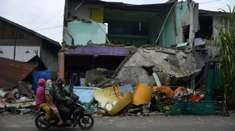 Pengendara melintas di sekitar sebuah rumah yang rusak akibat gempa bumi di Kabupaten Mamuju, Sulawesi Barat, Minggu (17/1/2021).  ANTARA FOTO/Abriawan Abhe