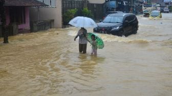 Warga melintasi jalan yang tergenang banjir di Desa Mejobo, Mejobo, Kudus, Jawa Tengah, Selasa (19/1/2021). [ANTARA FOTO]