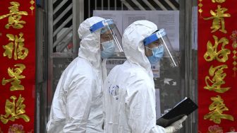 Petugas kesehatan berbicara dengan seorang penduduk di belakang gerbang luar blok apartemen saat melakukan pengujian di daerah Yordania, Hong Kong, Sabtu (23/1/2021). [Peter PARKS / AFP]