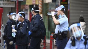 Seorang polisi (kedua dari kanan) minum di area yang ditutup oleh petugas kesehatan yang melakukan pengujian di daerah Yordania, Hong Kong, Sabtu (23/1/2021). [Peter PARKS / AFP]