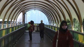 Warga mengenakan masker berjalan di jembatan penyeberangan orang (JPO) di kawasan Pasar Minggu, Jakarta, Selasa (26/1/2021). [Suara.com/Angga Budhiyanto]