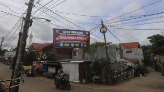 Pengendara sepeda motor melintas di dekat spanduk peringatan Zona Merah di Kelurahan Cipinang Melayu, Jakarta, Kamis (28/1/2021). [Suara.com/Angga Budhiyanto]