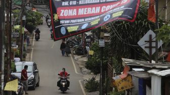 Pengendara sepeda motor melintas di dekat spanduk peringatan Zona Merah di Kelurahan Cipinang Melayu, Jakarta, Kamis (28/1/2021). [Suara.com/Angga Budhiyanto]