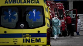 Petugas kesehatan berjalan di samping lusinan ambulans yang menunggu di luar layanan darurat COVID-19 di Rumah Sakit Santa Maria, Lisbon, pada (28/1/2021). [PATRICIA DE MELO MOREIRA / AFP]