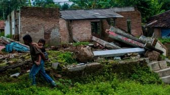 Seorang bapak menggendong anaknya melintas di puing-puing rumah yang ambruk akibat tanah bergerak di Desa Sudamanik, Lebak, Banten, Senin (1/2/2021). ANTARA FOTO/Muhammad Bagus Khoirunas