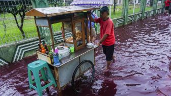 Pedagang bakso berjalan di jalan perkampungan yang tergenang banjir berwarna merah di Jenggot, Pekalongan, Jawa Tengah, Sabtu (6/2/2021). [ANTARA FOTO/Harviyan Perdana Putra]