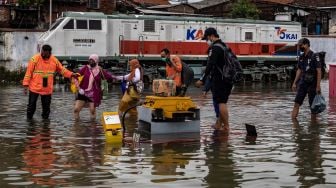 Karyawan membantu sejumlah penumpang menembus banjir untuk keluar dari Stasiun Tawang yang terendam banjir di Semarang, Jawa Tengah, Sabtu (6/2/2021). [ANTARA FOTO/Aji Styawan]
