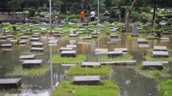 Warga melihat area pemakaman yang terendam banjir di TPU Karet Bivak, Jakarta Pusat, Minggu (7/2/2021). [Suara.com/Alfian Winanto]