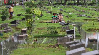 Anak - anak bermain di area pemakaman yang terendam banjir di TPU Karet Bivak, Jakarta Pusat, Minggu (7/2/2021). [Suara.com/Alfian Winanto]