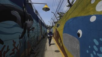 Seorang warga berjalan di depan mural bertema kehidupan laut di Kampung Lodan, Jakarta, Senin (8/2/2020). [Suara.com/Angga Budhiyanto]