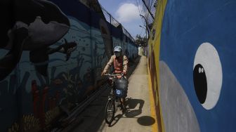 Seorang warga bersepeda melintas di depan mural bertema kehidupan laut di Kampung Lodan, Jakarta, Senin (8/2/2020). [Suara.com/Angga Budhiyanto]