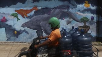 Pengedara sepeda motor melintas di depan mural bertema kehidupan laut di Kampung Lodan, Jakarta, Senin (8/2/2020). [Suara.com/Angga Budhiyanto]