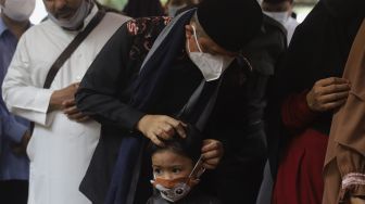 Ustadz Yusuf Mansur membetulkan masker yang dikenakan oleh anak pertama Almarhum Ustadz Maaher At-Thuwailibi saat prosesi pemakaman di Kompleks Pemakaman Pondok Pesantren Daarul Quran, Cipondoh, Tangerang, Banten, Selasa (9/2/2021). [Suara.com/Angga Budhiyanto]