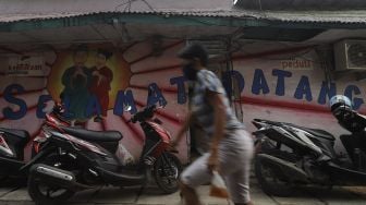 Warga berjalan di depan mural selamat datang di Kampung Tehyan, Kota Tangerang, Banten, Selasa (9/2/2021). [Suara.com/Angga Budhiyanto]