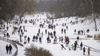 Sejumlah warga memanfaatkan salju untuk meluncur menggunakan kereta luncur mereka dan bermain di kolam beku di taman Wilmersdorf-Schoeneberg, distrik Schoeneberg, Berlin, pada (8/2/2021). [Odd ANDERSEN / AFP]