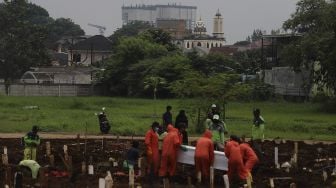 Petugas pemakaman membawa peti jenazah korban COVID-19 di TPU Bambu Apus, Jakarta Timur, Sabtu (13/2/2021). [Suara.com/Angga Budhiyanto]