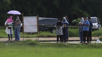 Keluarga memanjatkan doa saat menyaksikan dari kejauhan pemakaman jenazah korban COVID-19 di TPU Bambu Apus, Jakarta Timur, Sabtu (13/2/2021). [Suara.com/Angga Budhiyanto]