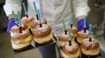 Seorang karyawan berpose dengan berliners (donat Jerman) dengan jarum suntik penuh jeli raspberry yang diproduksi oleh toko roti Kreyenbuhl, Muri, Swiss, pada (5/2/2021). [STEFAN WERMUTH / AFP]