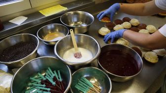 Seorang karyawan menyiapkan berliner (donat Jerman) yang akan dijual dengan jarum suntik penuh jeli raspberry di toko roti Kreyenbuhl, Muri, Swiss, pada (5/2/2021). [STEFAN WERMUTH / AFP]