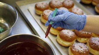 Seorang karyawan menyiapkan berliner (donat Jerman) yang akan dijual dengan jarum suntik penuh jeli raspberry di toko roti Kreyenbuhl, Muri, Swiss, pada (5/2/2021). [STEFAN WERMUTH / AFP]