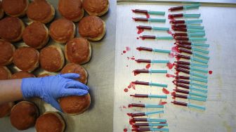 Seorang karyawan memegang berliner (donat Jerman) di dekat jarum suntik yang penuh dengan jeli raspberry di toko roti Kreyenbuhl, Muri, Swiss, pada (5/2/2021). [STEFAN WERMUTH / AFP]