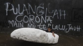 Seorang anak bermain menggunakan styrofoam saat banjir merendam kawasan Kemang Utara, Jakarta, Kamis (18/2/2021). [Suara.com/Angga Budhiyanto]