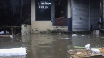 Seorang warga duduk di salah satu kios saat banjir merendam kawasan Kemang Utara, Jakarta, Kamis (18/2/2021). [Suara.com/Angga Budhiyanto]