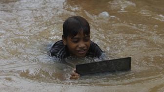 Seorang anak bermain air saat banjir merendam Kelurahan Cipinang Melayu, Jakarta, Jumat (19/2/2021). [Suara.com/Angga Budhiyanto]