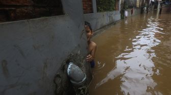 Seorang anak bermain di dekat rumahnya yang terendam banjir di Cipinang Muara, Jakarta, Jumat (19/2/2021). [Suara.com/Angga Budhiyanto]