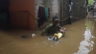 Seorang warga berjalan melintasi banjir yang merendam Kelurahan Cipinang Muara, Jakarta, Jumat (19/2/2021). [Suara.com/Angga Budhiyanto]