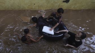 Sejumlah anak bermain air saat banjir merendam Kelurahan Cipinang Muara, Jakarta, Jumat (19/2/2021). [Suara.com/Angga Budhiyanto]