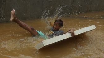 Seorang anak bermain air saat banjir merendam Kelurahan Cipinang Melayu, Jakarta, Jumat (19/2/2021). [Suara.com/Angga Budhiyanto]