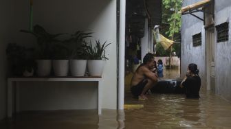 Warga beraktivitas di depan rumahnya yang terendam banjir di Cipinang Muara, Jakarta, Jumat (19/2/2021). [Suara.com/Angga Budhiyanto]