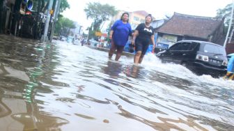 Warga melintas di Jalan Jatinegara Barat, Jakarta Timur yang tersendat akibat sebagian badan jalan terendam banjir luapan Sungai Ciliwung dengan ketinggian sekitar 20 sentimeter, Sabtu (20/2). [Suara.com/Oke Atmaja]
