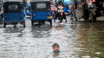 Bocah berenang di Jalan Jatinegara Barat, Jakarta Timur yang tersendat akibat sebagian badan jalan terendam banjir luapan Sungai Ciliwung dengan ketinggian sekitar 20 sentimeter, Sabtu (20/2). [Suara.com/Oke Atmaja]
