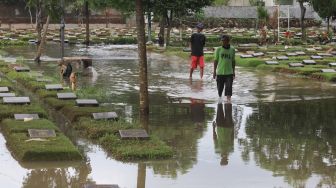 Warga melintas di sekitar area makam yang terendam banjir di TPU Jeruk Purut, Jakarta Selatan, Sabtu (20/2/2021). [Suara.com/Alfian Winanto]