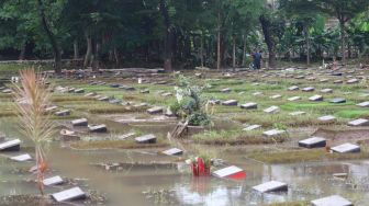 Petugas beraktivitas di sekitar area makam yang terendam banjir di TPU Jeruk Purut, Jakarta Selatan, Sabtu (20/2/2021). [Suara.com/Alfian Winanto]