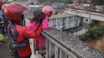 Seorang pengendara motor mengajak anaknya untuk menonton banjir dan aliran kali Ciliwung yang meluap dari atas Flyover Kalibata, Jakarta Selatan, Sabtu (20/2/2021). [Suara.com/Alfian Winanto]