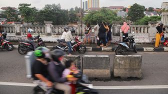 Sejumlah warga dan pengendara motor menonton banjir dan aliran kali Ciliwung yang meluap dari atas Flyover Kalibata, Jakarta Selatan, Sabtu (20/2/2021). [Suara.com/Alfian Winanto]