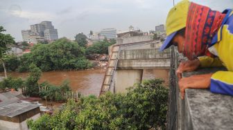 Seorang warga menonton banjir dan aliran kali Ciliwung yang meluap dari atas Flyover Kalibata, Jakarta Selatan, Sabtu (20/2/2021). [Suara.com/Alfian Winanto]